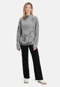 Grau gemusterter Pullover mit langen Ärmeln und hohem Kragen, kombiniert mit schwarzen weiten Hosen und weißen Sneakers.
