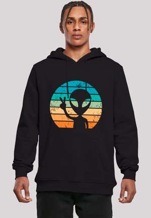 Schwarzer Hoodie mit einer runden Grafik, die einen silhouettierten Alien vor einem Farbverlauf aus blauen und orangefarbenen Streifen zeigt. Mit Kängurutasche vorne.