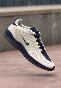 Nike-sneaker med en kremfarget overdel, marineblå aksenter, grønt logo, teksturert stoff og perforerte detaljer. Gummisåle med en buet design.