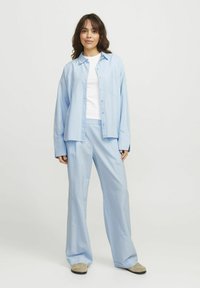 Zila svītrota krekla ar brīvu piegriezumu, pogām priekšpusē un krūšu kabatu, apvienojums ar saskaņojošām platajām biksēm un bezkrāsainām kurpēm.