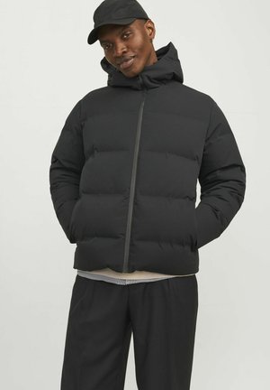 Chaqueta de plumas negra con cierre delantero, cuello alto y capucha. Presenta secciones acolchadas, textura suave y bolsillos laterales ocultos.