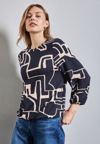 Top bleu marine avec un motif abstrait beige, encolure ronde et manches trois-quarts. Tissu doux avec une texture subtile. Assorti à un jean bleu.