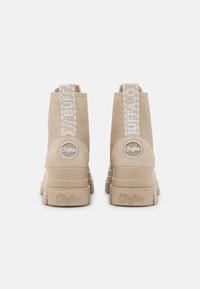 Stivaletti beige alla caviglia con finitura testurizzata, caratterizzati da un'etichetta con logo e un'etichetta a strappo decorata, montati su una suola spessa.