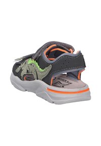 Sandale noire avec un design de dinosaure gris et vert, accents orange, bande velcro et semelle intérieure rembourrée, dotée d'une semelle en caoutchouc texturé.