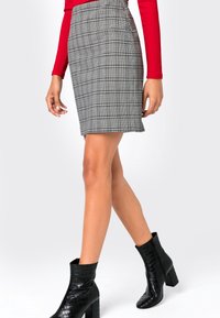 Grå rutmönstrad pennkjol med en figurnära design, i kombination med svarta ankelsboots i krokodilpräglat läder. Har en smal silhuett och knälång längd.