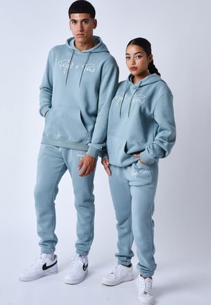 Des sweat-shirts bleu clair et des pantalons de jogging assortis en tissu doux, avec des poches avant et des accents de logo discrets, portés avec des baskets blanches.