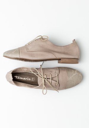 Chaussures en daim beige avec un embout en argent texturé et un laçage. Elles présentent un talon bas et des détails de couture subtils.