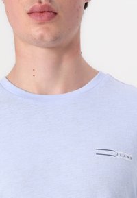 Šviesiai mėlynas medvilninis marškinėliai su apvaliu iškirpimu ir trumpomis rankovėmis, puošti mažai išsiuvinėtu "TOMMY JEANS" logotipu ant krūtinės.