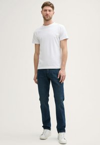 Camiseta de algodón blanca combinada con jeans de mezclilla azul oscuro. El conjunto se complementa con zapatillas blancas, creando una apariencia casual.