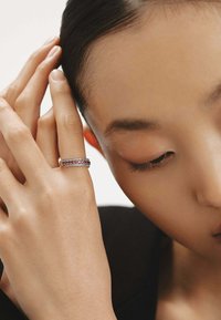 Anillo de plata con múltiples hileras de piedras preciosas claras y rosas alternadas, llevado en una mano de piel clara y textura suave.