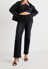 Svarta denimjeans med rakt ben, med stängd midja, framfickor och en slät, något texturerad yta.