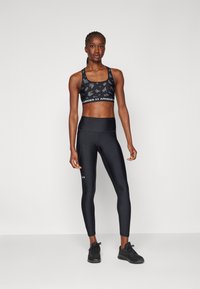 Melnā sporta krūšturis ar faktūru, uz kura redzama balta Under Armour logo. Melnās augstās gurnu leggingas, ar gludu apdari un pieguļošu formu.