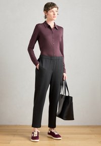 Chemise bordeaux à manches longues avec des boutons, associée à un pantalon à rayures charbon. Un sac tote noir et des baskets bordeaux avec des lacets crème complètent le look.