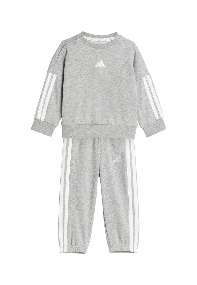 Grå sweatshirt och byxor, tillverkade av mjukt tyg. Har vita ränder på ärmarna och byxorna, med en liten logotyp på bröstet och låret.