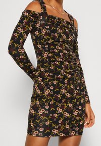 Černé květinové šaty s dlouhými rukávy a odhalenými rameny. Texturovaná látka s nashromážděnými detaily a vícebarevnými květinovými vzory.