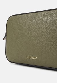 Borsa in pelle verde oliva con texture, con bordi neri e logo del marchio dorato nell'angolo in basso a destra. Superficie liscia con leggera grana.