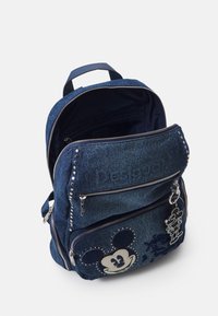 Granatowy plecak z dżinsowego materiału ozdobiony srebrnymi ćwiekami, z podwójnymi kieszeniami na zamek oraz wzorami Mickey Mouse. Posiada wytrzymałe paski i uchwyt u góry.