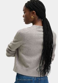 Grå stickad tröja med rund halslinning, ribbade ärmslut och nederkant samt en mjuk textur. Matchas med blå denim, vilket visar en informell stil.