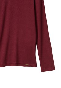 Bordeauxfarbendes Langarmhemd aus weichem, strukturiertem Stoff mit rundem Ausschnitt und einem kleinen Metallschriftzug nahe dem Saum.