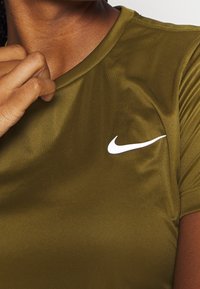 Olivgrön träningsskjorta i mjukt, stretchigt material, med en vit Nike-logotyp på vänster bröst och rundad halsringning.