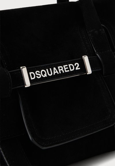 Gros plan d’un sac noir avec une plaque en métal argenté portant le nom de la marque DSQUARED2 en lettres blanches.