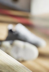 Baskets grises avec un matériau texturé et des semelles blanches, légèrement floues en arrière-plan, reposant sur une surface en bois.