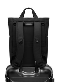 Fekete hátizsák párnázott vállpántokkal és egy felső fogantyúval, amely a poggyászhoz rögzíthető. Simaság jellemzi, látható minták nélkül.