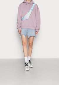 Sudadera lavanda con capucha y cordones, combinada con una falda de mezclilla desgastada. Zapatillas blancas y calcetines blancos holgados completan el conjunto.