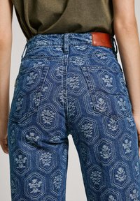 Modré džínsy z denimu s kvetinovým embosovaným vzorom, piatimi vreckami a hnedou koženou nášivkou na páse. Klasický strih rovného nohavice.