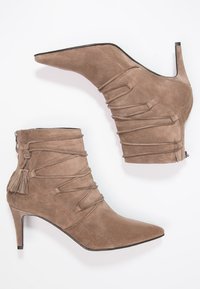 Botines de ante marrón hasta el tobillo con punta afilada, que cuentan con detalles arrugados, un cierre lateral y un tassel decorativo en la parte posterior.