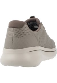 Zapatilla deportiva de color gris claro con parte superior de malla texturizada, cuello acolchado y suela blanca gruesa. Presenta detalles y marca en gris minimalistas.