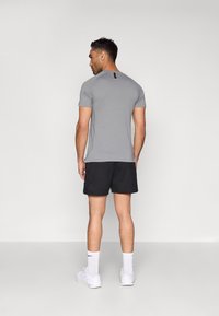 Szürke rövid ujjú ing fekete díszítésekkel, fekete rövidnadrággal párosítva. A modell laza szabást mutat, a funkcionalitásra és a kényelemre helyezve a hangsúlyt.