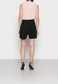 Sorte cargo shorts med sidelommer, parret med en lyserød ærmeløs top. Outfitet komplimenteres af sorte højhælede sko.