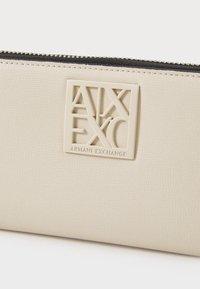 Bežna faux usnjena denarnica z teksturirano površino, črn zadrgo in izstopajočo označbo z logotipom "Armani Exchange".