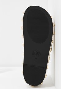 Semelle en caoutchouc noir d'une chaussure sans lacets avec des bords cloutés et "River Island 4" embossé au centre.