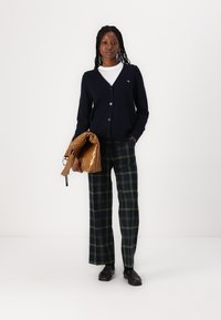 Navy cardigan with buttons, white t-shirt underneath, green and black plaid wide-leg trousers, and a shiny brown handbag. Black shoes.