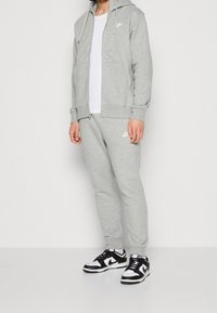 Grå zip-hoodie med dragsko och sidofickor, tillsammans med matchande grå joggers. Svart-vita Nike-sneakers fulländar looken.