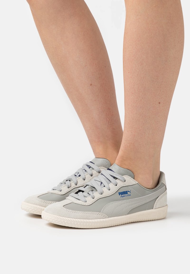 Jasnoszare sneakersy z zamszu i skóry syntetycznej. Okrągły nosek, wyściełany kołnierz i gumowa podeszwa. Zawierają granatowe logo i sznurowadła.