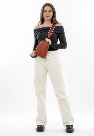Bolso bandolera marrón texturizado con forma redondeada, correa ajustable, bolsillo delantero con cremallera y un logo sutil. Llevado por una persona.