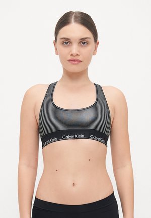 Svart og hvit stripet sports-bh med en bred elastikkant som viser Calvin Klein-logoen. Rundt utringning og racerback-design.