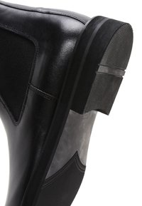Stivaletto nero con pelle liscia, suola in gomma testurizzata e pannelli laterali elastici. Punta arrotondata e elementi di design minimalisti.