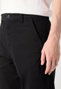 Black cotton trousers with a straight cut, featuring a button closure, side pockets, and visible stitching detail along the seams.