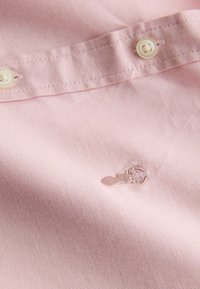 Šviesiai rožinė audinys su tekstūruota paviršiaus struktūra, su mažu siuvinėtu raštu ir sagute ant apykaklės.