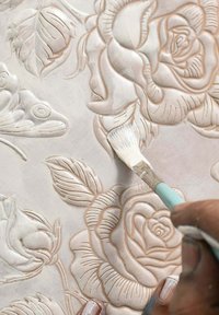 Textured reliefpaneel met rozen- en bladmotieven in zacht beige. Een penseel brengt een lichte kleur aan op het gegraveerde ontwerp om details te accentueren.