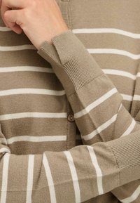 Lett cardigan i beige med hvite horisontale striper, med ribbestrikkede mansjetter og knappeåpning foran. Myk tekstur.