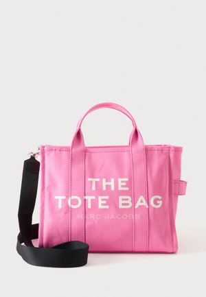 Sac cabas en toile rose avec deux anses et une bandoulière noire, avec le texte blanc « THE TOTE BAG MARC JACOBS » sur le devant.