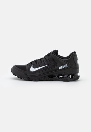Baskets de sport noires avec logo blanc en forme de virgule, texte « REAX » sur le côté, semelle amortissante et design à lacets sur fond clair uni.