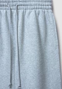 Pantaloni da allenamento grigi chiari con vita elastica e lunghi lacci che pendono al centro davanti.