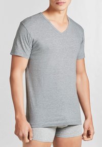 T-shirt grigio a maniche corte con scollo a V, realizzato in tessuto morbido, caratterizzato da una vestibilità ampia e una texture liscia. Indossato con boxer leggeri grigi.