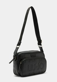 Melnā crossbody soma, kas izgatavota no teksturēta materiāla, ar rāvējslēdzēja galveno nodalījumu, izteiktiem logotipa akcentiem un regulējamu siksnu.